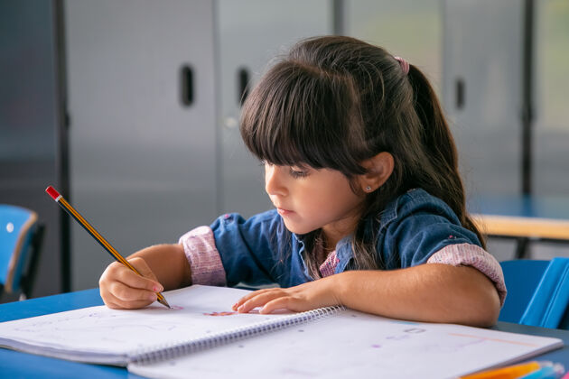 知识一个满头愁容的拉丁女孩坐在课桌旁 在抄写本上画画室内学校小学
