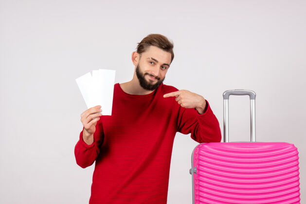 风景正面图：年轻男性 带着粉色包 手持机票 在白墙上航行 彩色旅行 度假照片微笑游客漂亮