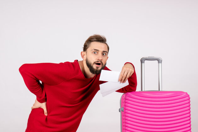 男人正面图：年轻男性 带着粉色包 手持白墙彩色旅行机票微笑度假年轻男性