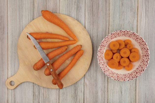 切碎顶视图橙色胡萝卜在一个木制的厨房板与切碎的胡萝卜在一个灰色的木制背景碗刀顶部蔬菜碗
