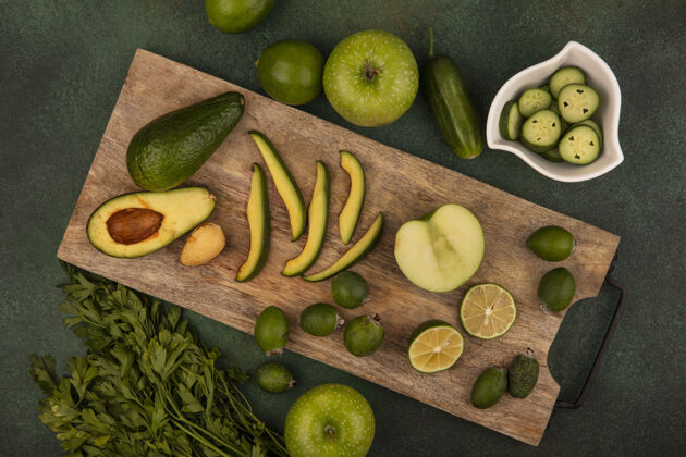 苹果健康鳄梨的俯视图 切片放在木制厨房板上 半青柠和切碎的黄瓜片放在碗上 青柠 青苹果和欧芹隔离在绿色背景上小吃木材肥肉
