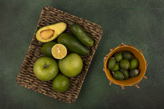 微笑一个柳条托盘的顶视图 新鲜食物 如青苹果 酸橙 鳄梨和黄瓜 绿色背景上的桶上有飞珠顶部托盘鳄梨