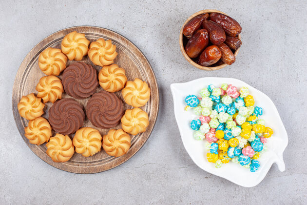 枣饼干放在木板上 旁边是一盘糖果和一碗枣子 背景是大理石高质量的照片烘焙饼干盘子