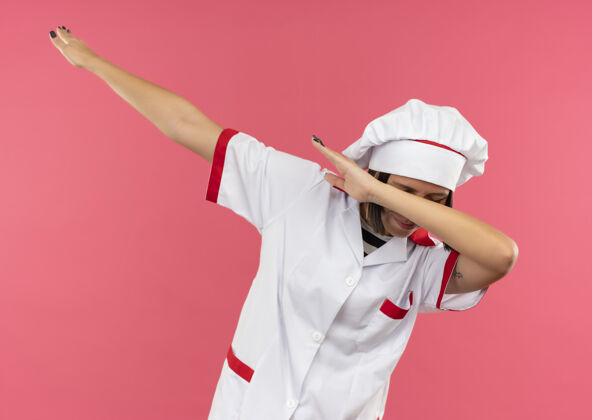 女性身着厨师制服的年轻女厨师在粉色背景上做着闭着眼睛的手势手势厨师轻拍