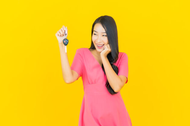 业主画像美丽的亚洲年轻女子微笑着把车钥匙放在黄色的墙上人购买旅游