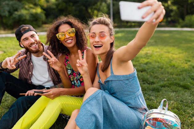 酷五彩缤纷时尚快乐的年轻朋友陪伴坐在公园里 男女同乐多种族太阳镜青春