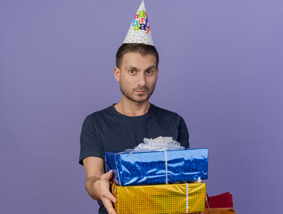 男人戴着生日帽的白种人帅哥拿着礼品盒和购物袋 紫色背景上有复印空间请拿着购物