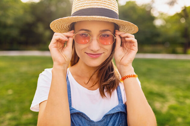 女性戴着草帽 戴着粉色太阳镜 微笑着行走在公园里的年轻漂亮女人的肖像 夏日时尚的风格 五颜六色的时髦装扮微笑年轻酷