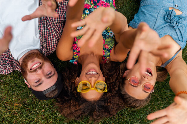 微笑俯瞰五颜六色时尚快乐的年轻朋友们躺在公园的草地上 男女同乐团结积极女人