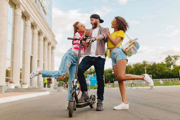 人快乐的年轻朋友们带着电动脚踏车走在街上 男女同乐阳光活动多样性