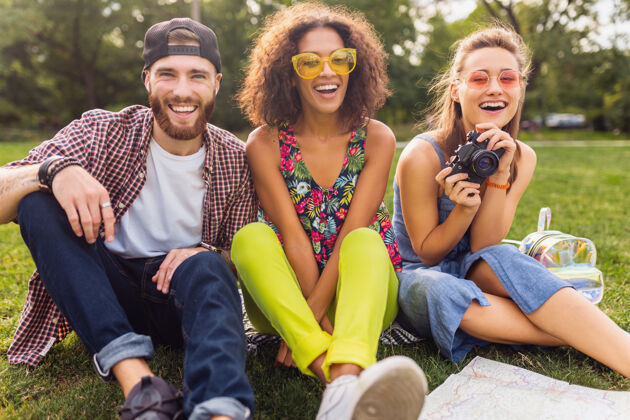 人快乐的年轻朋友们一起坐在公园里 男女同乐 带着相机旅行年轻女孩多民族
