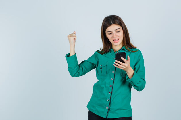 年轻人身着绿色衬衫的年轻女士看着手机 显示出赢家的姿态 看起来很幸运 正面视图喜悦女性欢笑