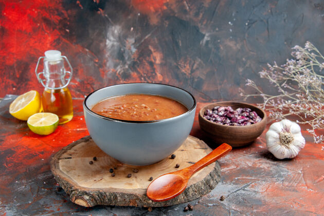 瓶子番茄汤的侧视图 勺子放在木托盘上 豆子油瓶和大蒜柠檬番茄放在五颜六色的桌子上热的容器碗