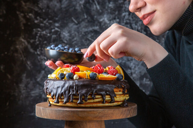 巧克力正面图美味的巧克力蛋糕被女性用水果装饰在黑暗的墙上糖人黑