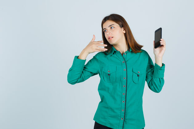 人身穿绿色衬衫的年轻女士指着手机 神情迷惑不解 前视图金发电话休闲