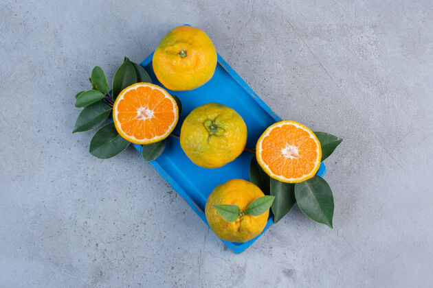天然橘子和叶子放在一个蓝色的小盘子里 背景是大理石美味营养水果