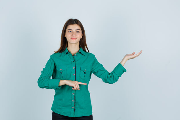 指向一幅年轻女士的肖像 她穿着绿色衬衫 一边表示欢迎 一边看着欢快的前景色现代女人表演