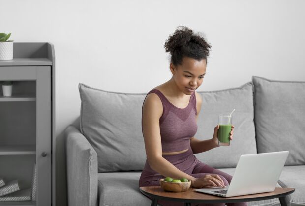 热带健身女士一边用笔记本电脑一边喝果汁水果热带水果准备