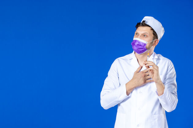 工作服身穿医疗服 戴着紫色口罩的男医生正对着蓝色的脸拿着针剂药品男医生医院