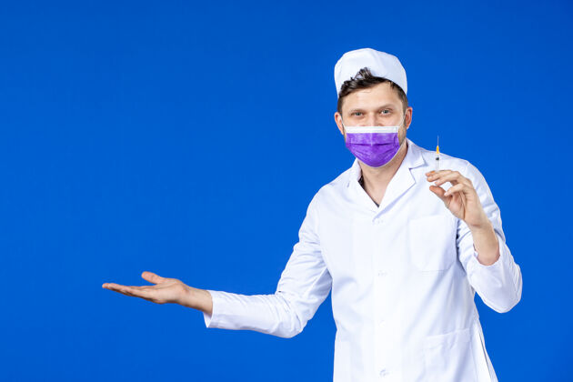 病毒前视图微笑的男医生穿着医疗服和面罩举行注射蓝色大流行医院注射