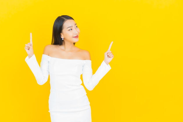 手臂在黄色的墙上 一位年轻漂亮的亚洲商业女性微笑着指着白色的裙子西装模特亚洲人