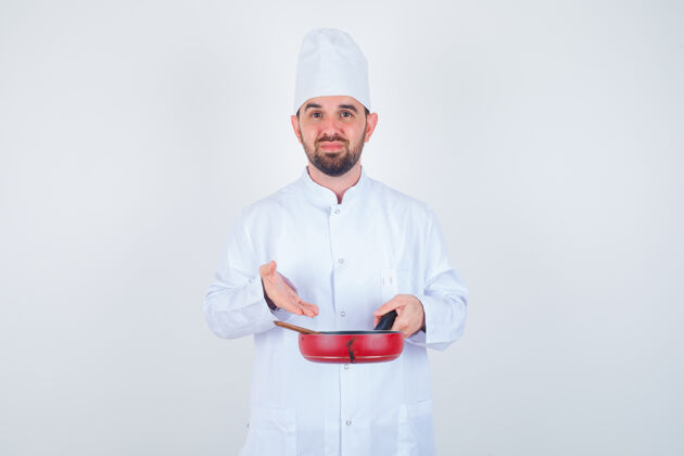 肖像年轻男厨师的肖像 展示空煎锅和木制勺子在白色制服和俯视前视图年轻平底锅薯条