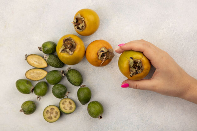 食物女性手拿着有机柿子水果的俯视图 灰色的表面上隔离着飞珠和柿子手配料新鲜