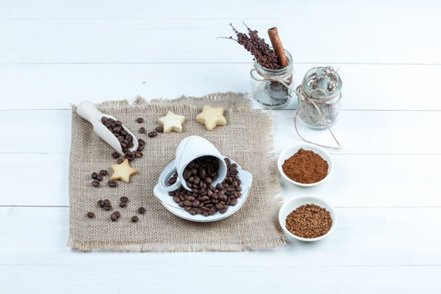 早餐星星饼干 咖啡豆放在一个袋子上 一碗速溶咖啡 一罐草药放在白色木板背景上特写浓缩咖啡笑碗