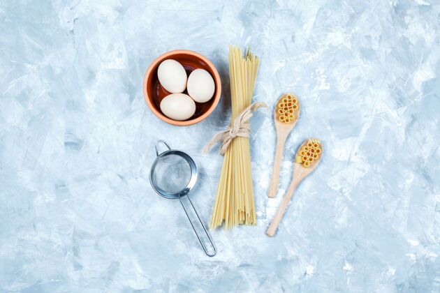 木头顶视图：木制汤匙中的意大利面 鸡蛋 粗灰色背景上的滤网水平菜肴饮食罗勒