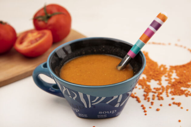 菜肴顶视图橙色小扁豆汤在一个碗与汤匙西红柿在一个木制的厨房板上的白色表面餐食物勺子