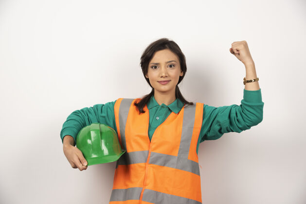 模特年轻的女工程师展示肌肉 手持白色背景的头盔女性专业建筑工人