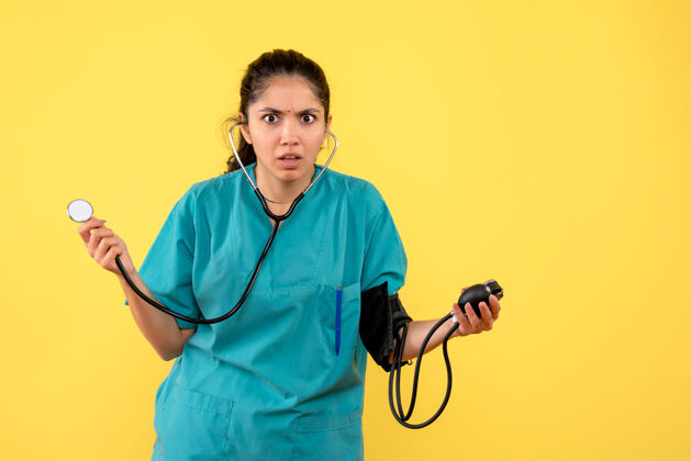医学前视图困惑的女医生穿着制服 用血压计站在黄色背景上人医院女医生