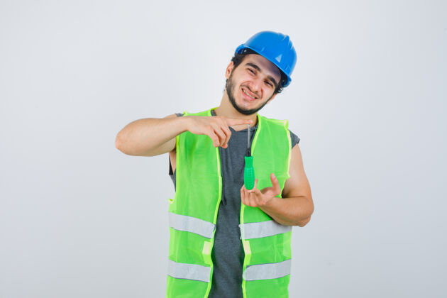 建筑工人年轻的建筑工人穿着制服 用螺丝刀显示尺寸标志 看上去很高兴 正面视图手势欢呼保护