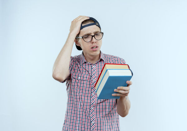 男性困惑的年轻学生男孩戴着眼镜和帽子拿着书看帽子戴男孩