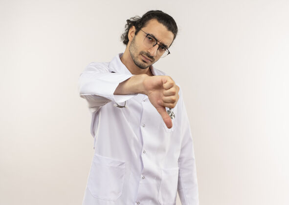 男性可怜的年轻男医生戴着眼镜 穿着白袍 听诊器 拇指朝下穿光学医生