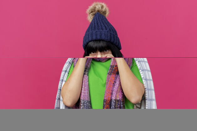 穿年轻生病的白人女孩戴着冬天的帽子 围着方格布围巾 在鼻子上贴上医用膏药 隔离在深红色的墙壁上 留着复印空间帽子围巾石膏