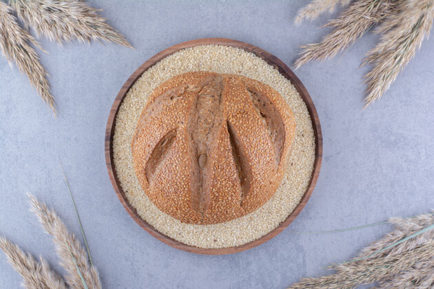 面团在一个装满芝麻籽的盘子里放一块面包 在大理石表面用干羽毛草茎围起来面包托盘面包屑