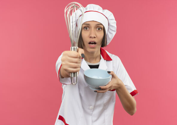 厨师令人印象深刻的年轻女厨师长在厨师制服伸展打蛋器和举行的粉红色与复制空间隔离碗年轻烹饪碗