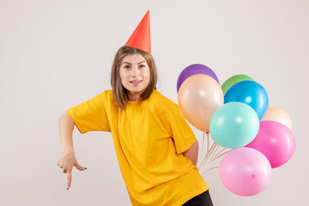 回来年轻的女性把彩色的气球藏在白色的背上气球聚会年轻女性