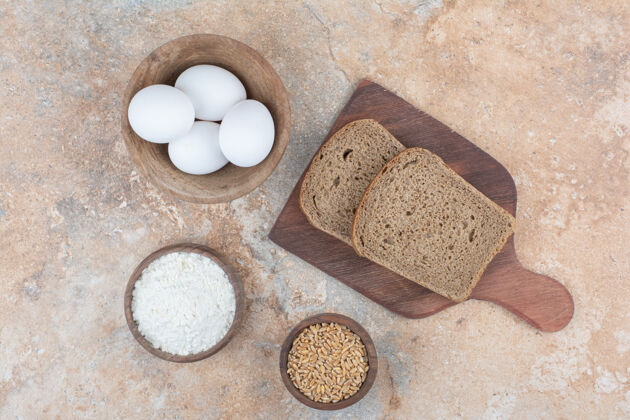 新鲜面包片 鸡蛋碗 面粉和大麦放在大理石表面面包黑麦碗