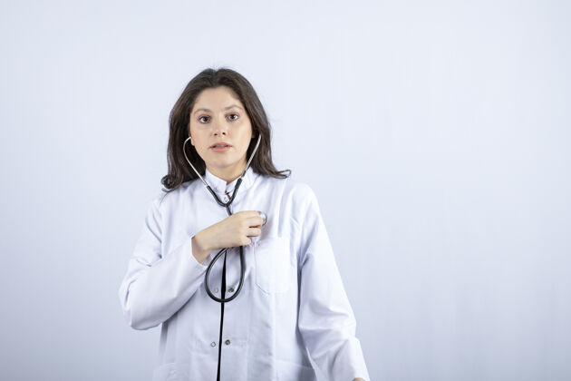 制服年轻女医生在白墙上用听诊器检查脉搏健康女性持有