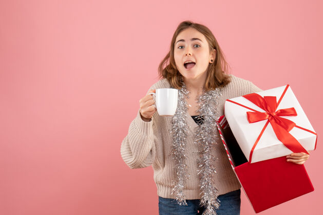 杯子年轻的女性拿着圣诞礼物盒和一杯粉红色的茶礼物时尚圣诞节