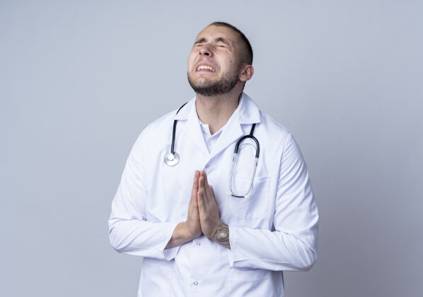 周围焦急的年轻男医生穿着医用长袍 脖子上戴着听诊器 双手做着祈祷的姿势 闭着眼睛 隔离在白色的空间里手医疗关闭