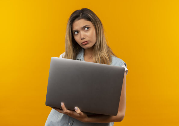 困惑迷茫的年轻漂亮的学生女孩戴着背包拿着笔记本电脑看着边上孤立的橙色与复印空间复制女孩壁板