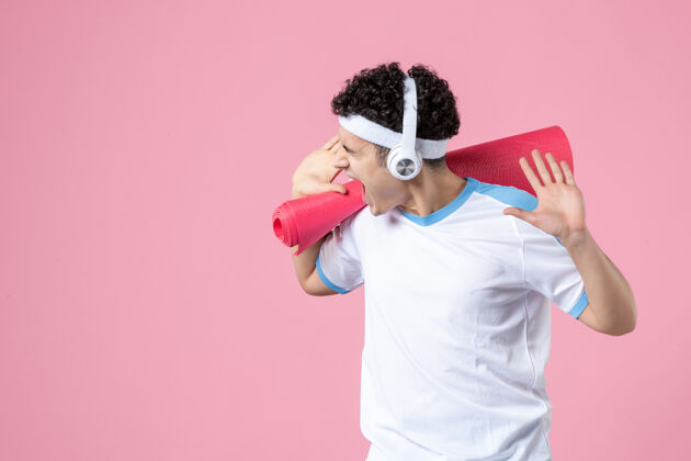 垫子正面图：穿着运动服的年轻男性 粉色墙上有瑜伽垫和耳机运动耳机年轻男性