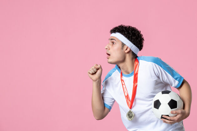 视图正面图身穿运动服的年轻男性 粉色墙上挂着足球前面足球球