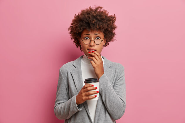 情绪忧心忡忡的成年美国黑人女商人陷入困境 在工作中搞得一团糟 咬嘴唇 看起来很尴尬 拿着一次性咖啡 穿着正式的衣服眼镜非洲裔女士