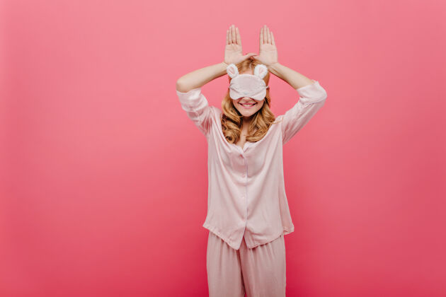 舒适穿着睡衣的漂亮女孩在粉红色的墙上嬉戏穿着睡衣的欧洲女士在睡前嬉戏的室内照片睡衣微笑睡衣