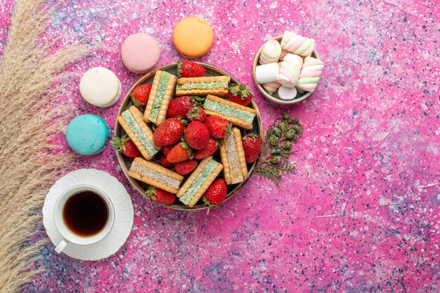 饼干美味的华夫饼干的顶视图 新鲜的红色草莓 麦卡龙和粉红色表面的茶食物美味糖果