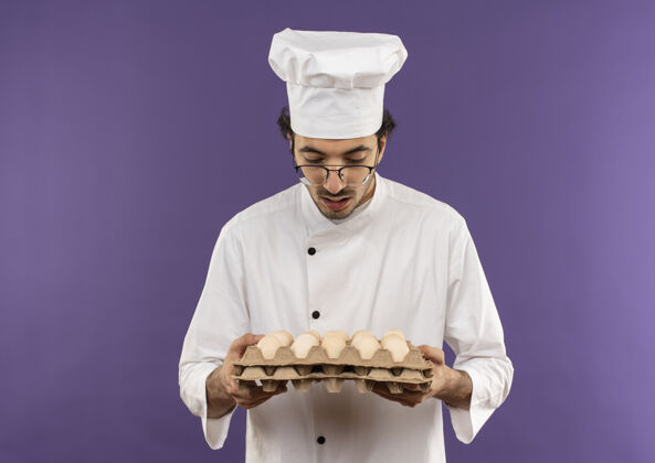 年轻年轻的男厨师穿着厨师制服 戴着眼镜 手里拿着一批紫色的鸡蛋背景紫色惊喜